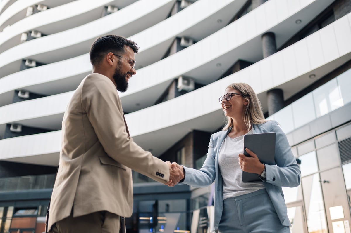 Two business partners shaking hands in front of an office building