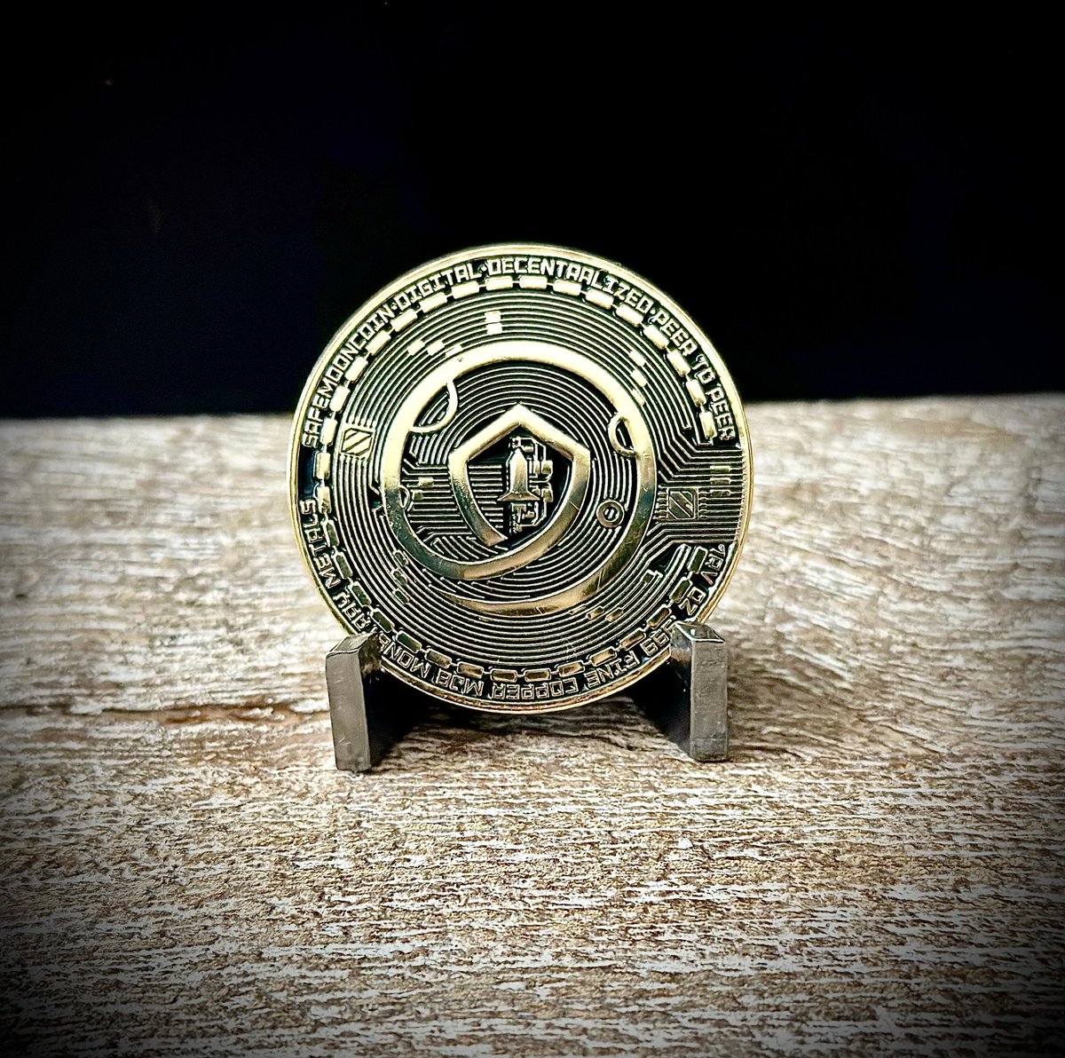 Gold challenge coin with engraved emblem displayed on stand against dark background